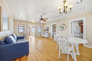 A spacious living area with a blue sofa, white dining table, and ceiling fans. - Phenomenal On Ocean Central Huge 4k sqft w Private Pool/Yard/Patio/Deck/Gameroom (North Myrtle Beach)