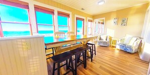 Ein Zimmer mit Holzboden, einer Bar mit Hockern, einer Couch und Blick durch große Fenster.