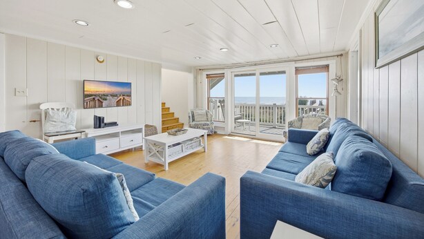 Un salón espacioso con un sofá grande, una mesa de centro y un televisor. Hay un balcón con vistas al mar.
