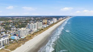 Un paisaje urbano costero con un hotel frente a la playa, edificios altos y una extensa playa de arena.
