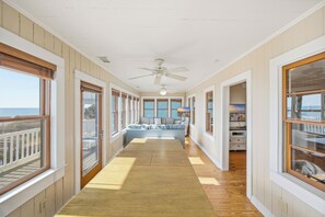 A corridor with a ceiling fan, large windows, a sofa, and a wooden floor.