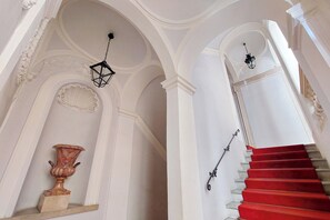 A grand staircase with red steps and white walls, ornate moldings, and a decorative vase. - Lavish apartment in historical building - Palazzo Boncompagni Corcos (Roma)