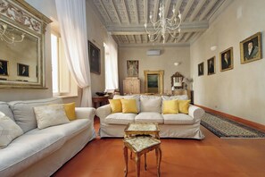 A living room with a sofa, a small table, a chandelier, and framed pictures on the walls. - Lavish apartment in historical building - Palazzo Boncompagni Corcos (Roma)