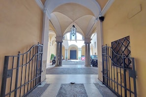 A corridor with arches, a central light fixture, and a gated entrance. - Lavish apartment in historical building - Palazzo Boncompagni Corcos (Roma)