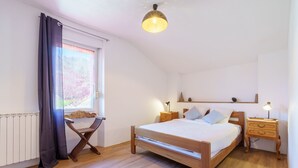 Un dormitorio con cama de madera, mesitas de noche, un radiador, una ventana con cortinas e iluminación en el techo.