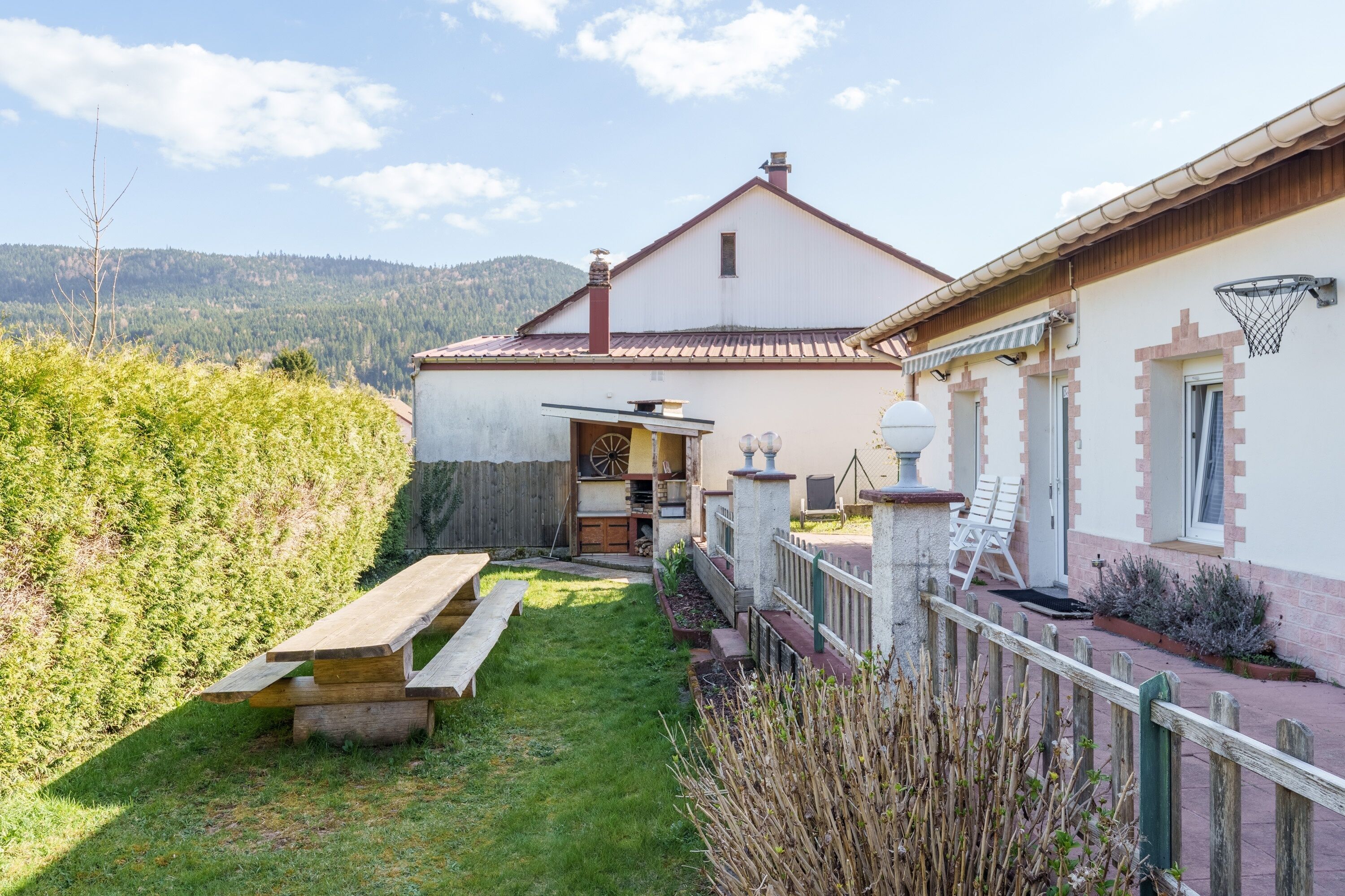A house with a patio, a wooden bench, a basketball hoop, and a view of the mountains.