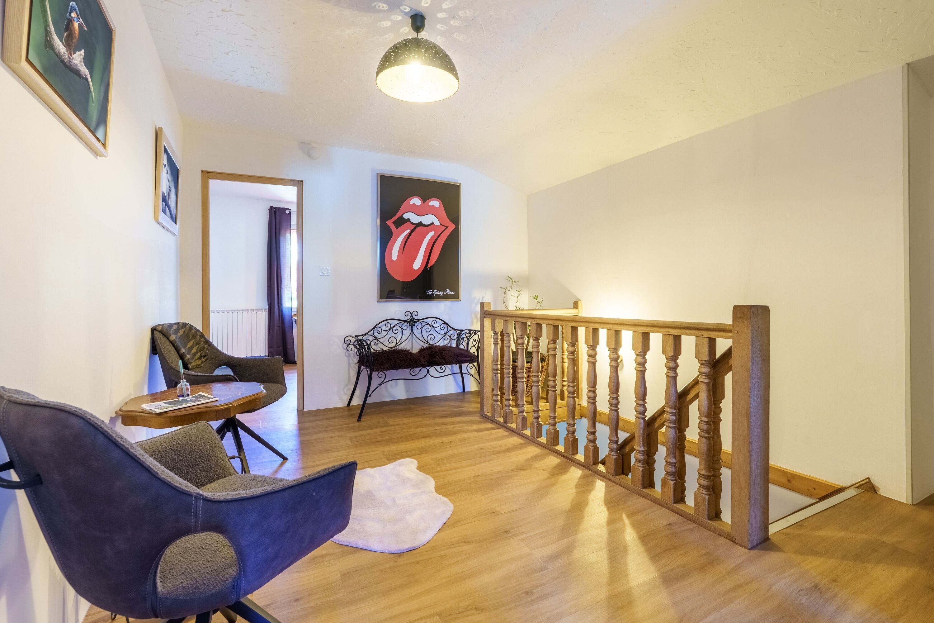 A room with a wooden floor, a staircase with a wooden railing, a black metal bench, and a framed artwork on the wall.