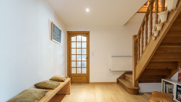 Una escalera de madera con barandilla, un banco de madera con cojines y una puerta con paneles de vidrio esmerilado.