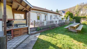 Una casa con zona de barbacoa, terraza de madera y jardín.