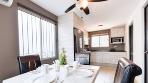 A dining area with a table set for two, a ceiling fan, a kitchen in the background, and a window with blinds. - 1 King, 3 Twin bed, Pool & 2 parking | 3BR2br 7ppl (Monterrey)
