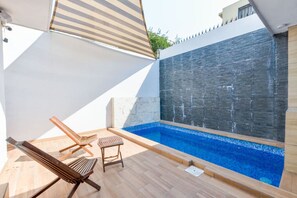 Une piscine extérieure équipée de deux chaises longues et d’un parasol.