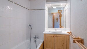 Een badkamer met witte betegelde wanden, een houten wastafelmeubel met een wastafel en een douchehoek.