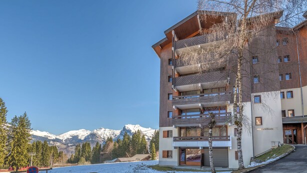 Een meerlaags hotel met balkons, een parkeerplaats en uitzicht op besneeuwde bergen.