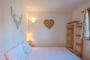 Ein Schlafzimmer mit einem Bett, einer Wandleuchte, einem herzförmigen Dekorationsobjekt und einem Holzbücherregal.