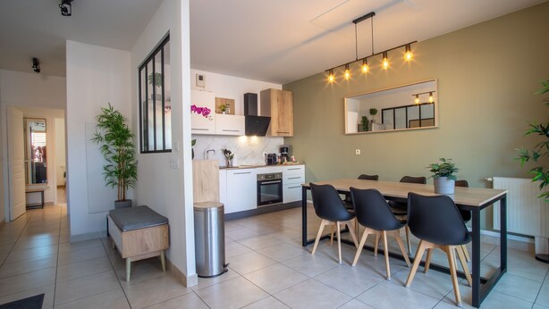 Una cocina moderna con armarios blancos, una mesa de comedor con sillas negras y un espejo grande sobre la mesa.
