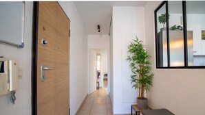 Un pasillo con puerta de madera, un banco, una planta en maceta y un espejo adosado a la pared.