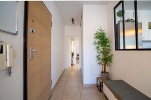 A hallway with a wooden door, a bench, a potted plant, and a wall-mounted mirror. - Cosy Green Bellevue - Avec balcon (Saint Etienne)