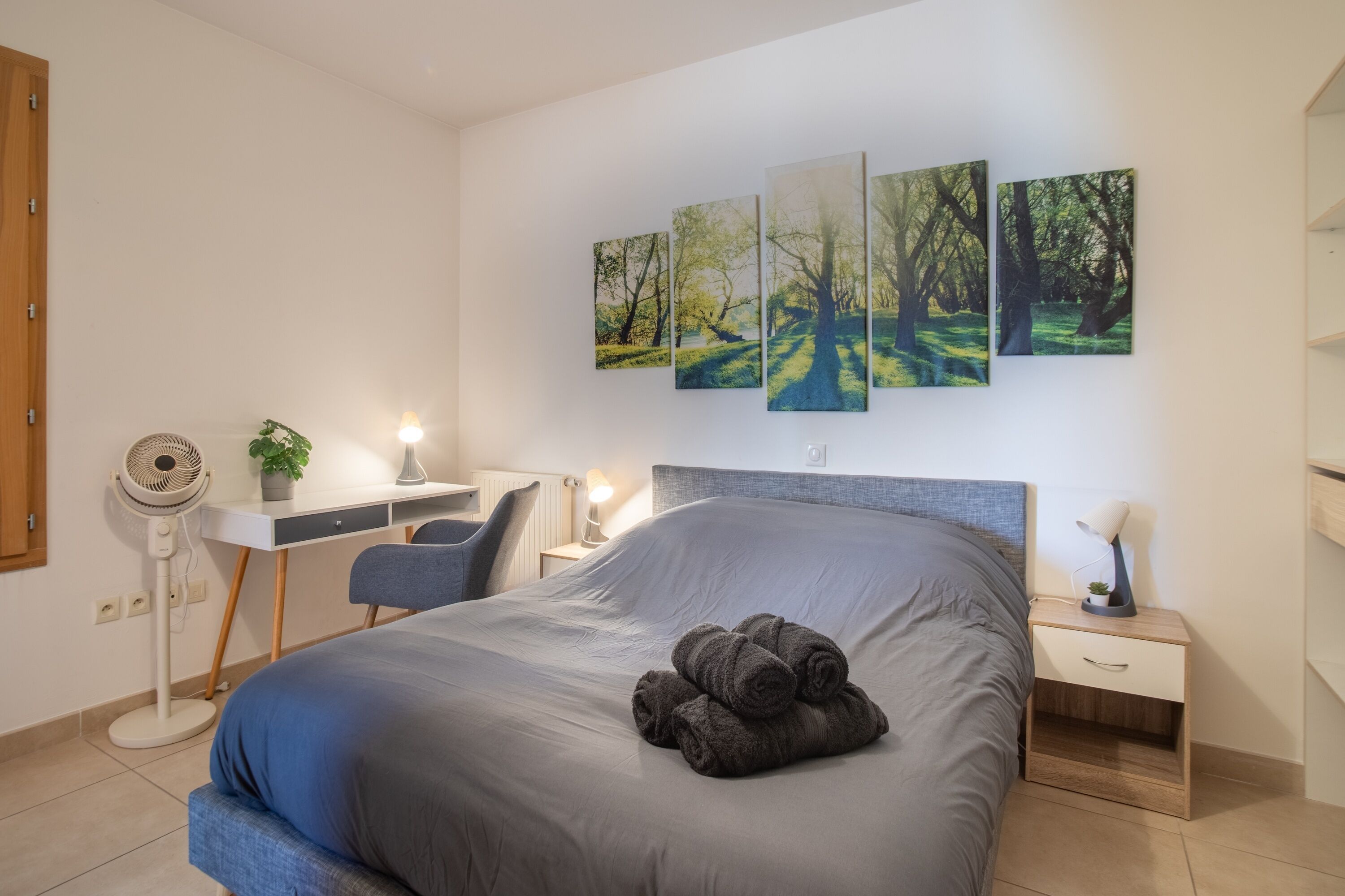 Ein Schlafzimmer mit Bett, Nachttisch, Schreibtisch, Stuhl und Wandbildern.