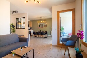 A modern living room with a sofa, a coffee table, and a dining area with chairs and a table. - Cosy Green Bellevue - Avec balcon (Saint Etienne)