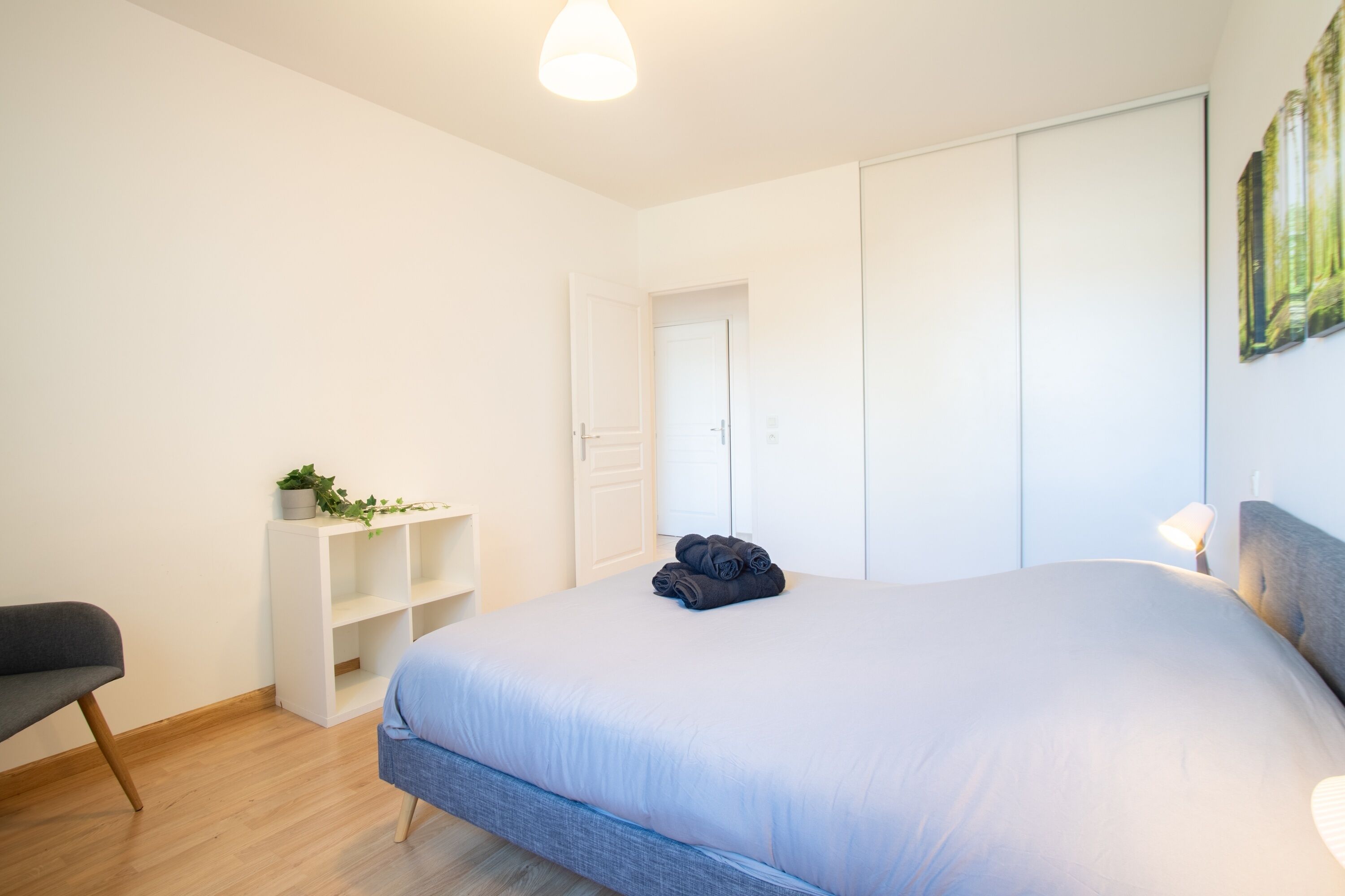 A bedroom with a bed, a chair, a shelf with a plant, and a wardrobe.
