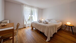 Een slaapkamer met een bed, nachtkastje met lamp, stoel en een raam met gordijnen.