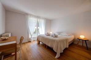 A bedroom with a bed, a bedside table with a lamp, a chair, and a window with curtains. - Villa Anahata - Avec Piscine Privée (La Teste-de-Buch)