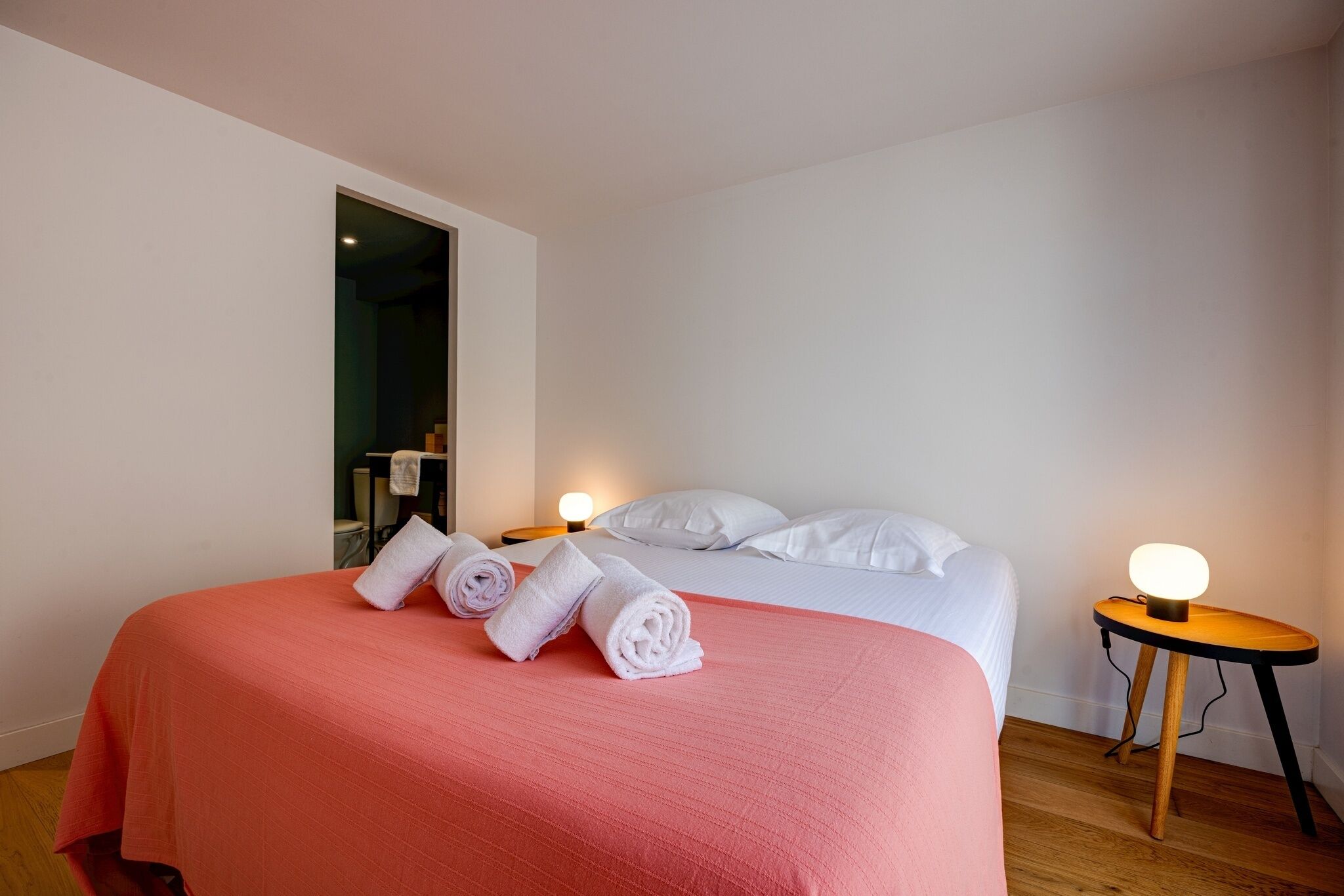 Hotellihuone, jossa on sänky, kaksi yöpöytää ja ovi, joka johtaa toiseen huoneeseen.