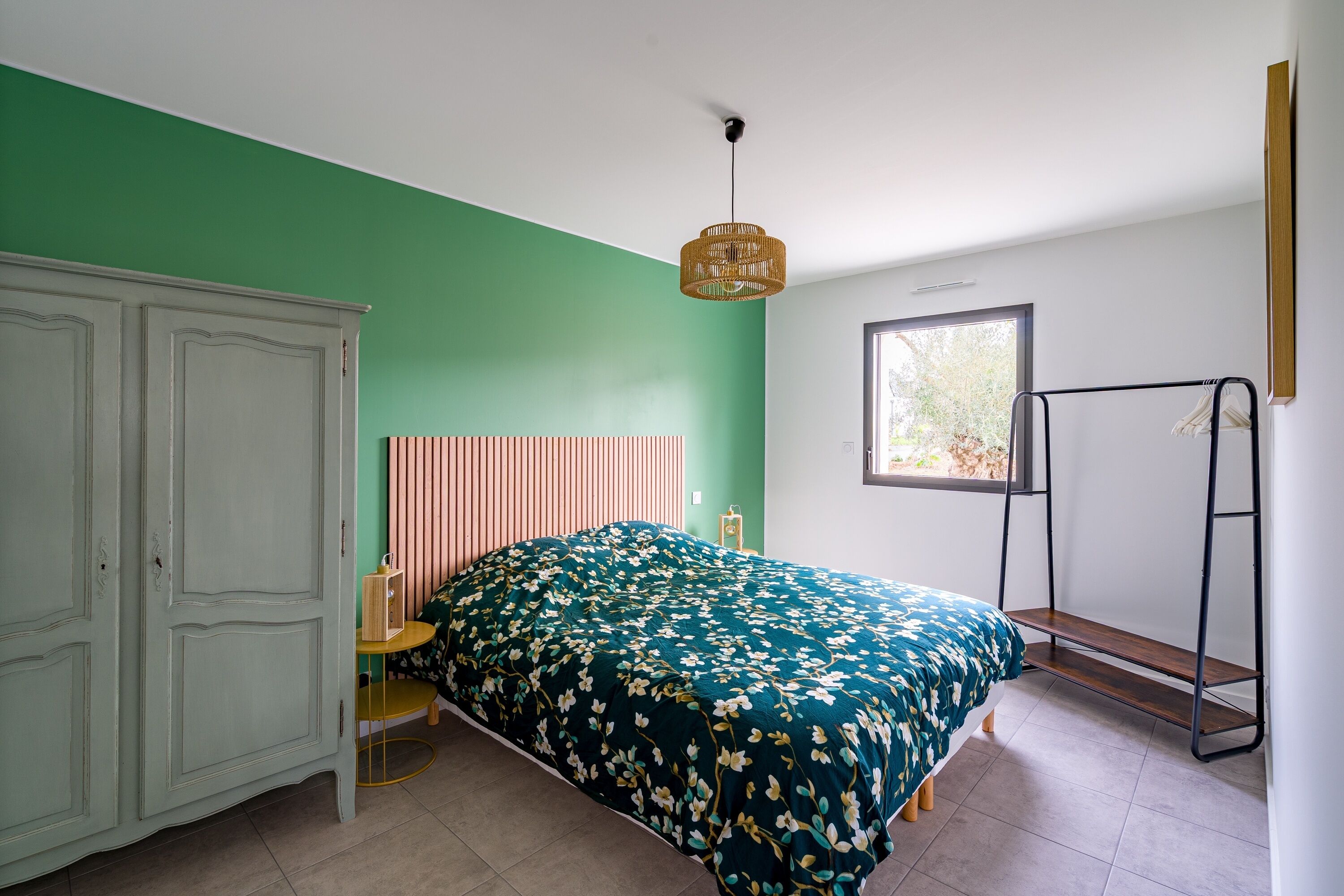 Ein Schlafzimmer mit Bett, Schrank, Fenster und einer Pendelleuchte.