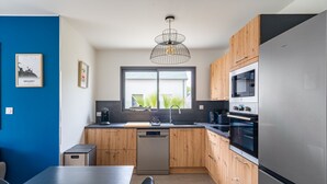 Ett modernt kök med träskåp, ett kylskåp i rostfritt stål, en diskmaskin och en hänglampa.