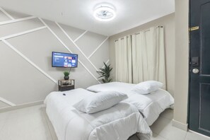 Een slaapkamer met een bed, een aan de muur bevestigde televisie, een klein tafeltje met een plant en een deur.