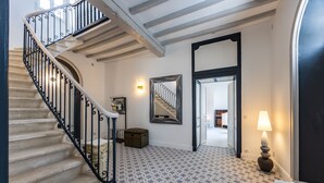 Una escalera con barandillas de hierro negro, suelo estampado, un espejo, una lámpara y un radiador.