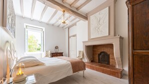 Un dormitorio con cama, mesita de noche, lámpara, chimenea y una ventana.
