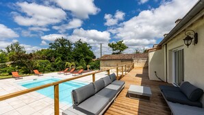 Zona de piscina con terraza de madera, sillas de descanso y una pileta.