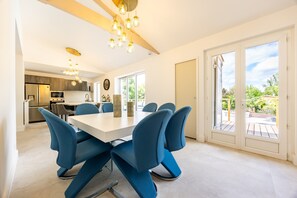 A modern kitchen with built-in appliances, a dining area with blue chairs, and large sliding glass doors leading to an outdoor patio. - Holiday Home “Le Domaine De Peyvideau” with Private Pool, Terrace, and Wi-Fi (Carignan-de-Bordeaux)