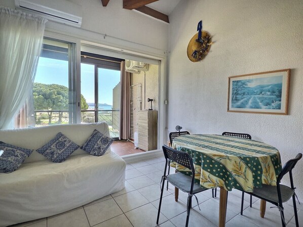 A room with a sofa, dining table, chairs, a painting, and a view through a sliding door.