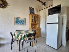 A compact kitchen with a dining table, chairs, a refrigerator, and a wooden cabinet.