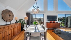 Uma sala de jantar espaçosa com um armário de madeira grande, uma mesa de jantar com cadeiras, uma planta em vaso e uma luminária pendente moderna.