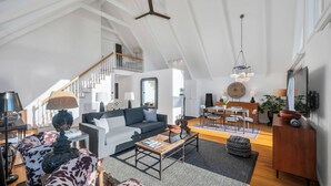 Um amplo loft com pé direito alto, escada, área de jantar e sala de estar mobiliada com sofás e mesa de centro.