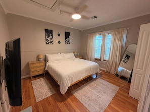Ein Schlafzimmer mit einem Bett, Nachttischen, einem Spiegel und einem Fenster mit Vorhängen.