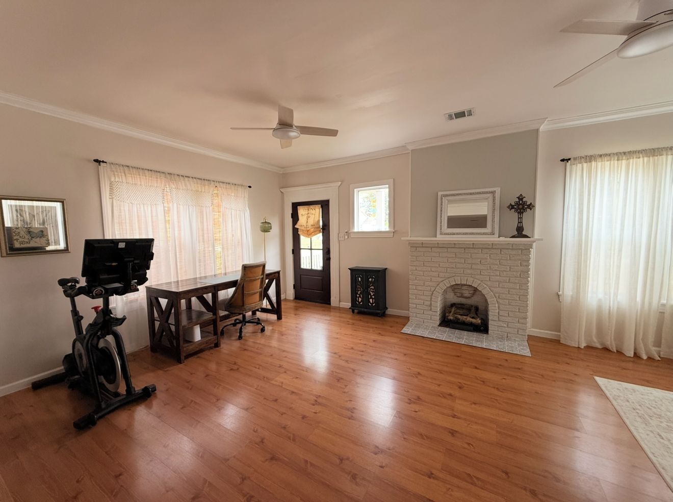 A spacious living room with hardwood flooring, a fireplace, a ceiling fan, and a dining area with a table and chairs.