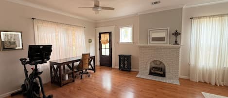 Amplia sala de estar con piso de madera, chimenea, ventilador de techo y comedor con mesa y sillas.