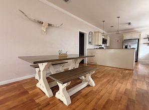 Ein Essbereich mit Holztisch und Bänken, im Hintergrund eine Küche und ein an der Wand befestigter Kuhsch ädel.