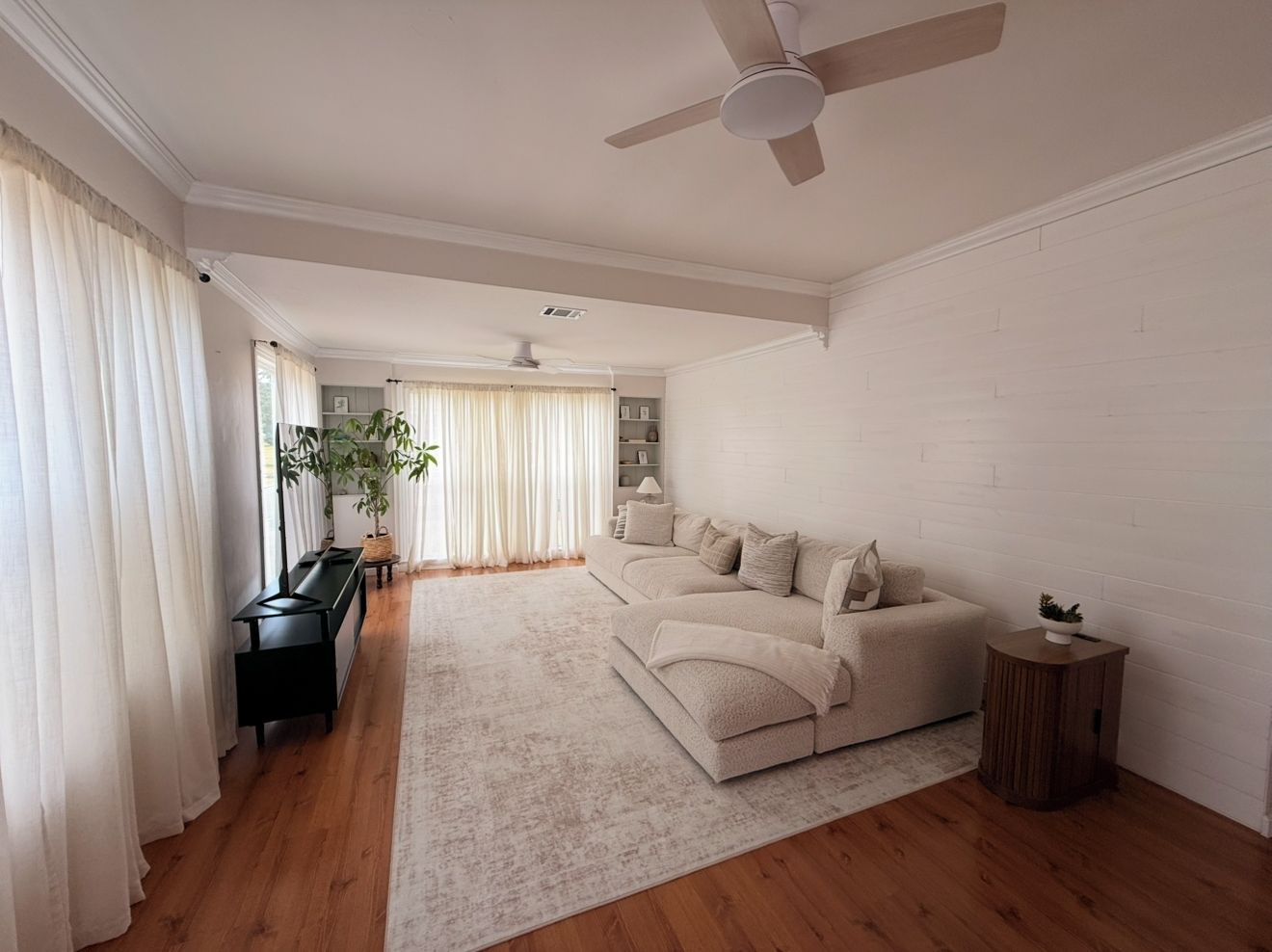 A spacious living room with a large sofa, a coffee table, and a ceiling fan.