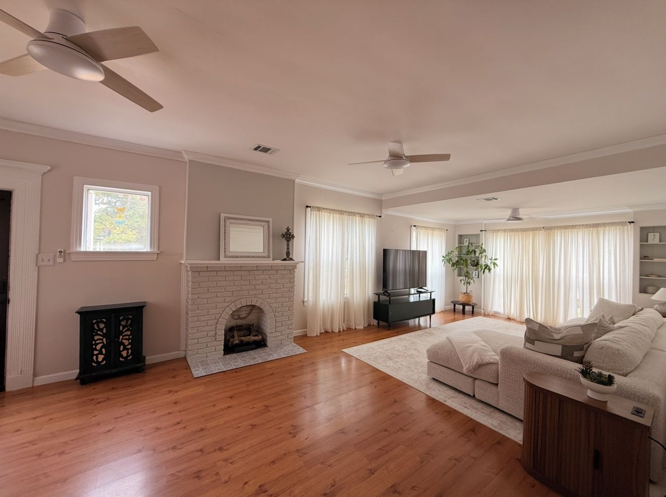 A spacious living room with hardwood flooring, a fireplace, a sofa, and a television.