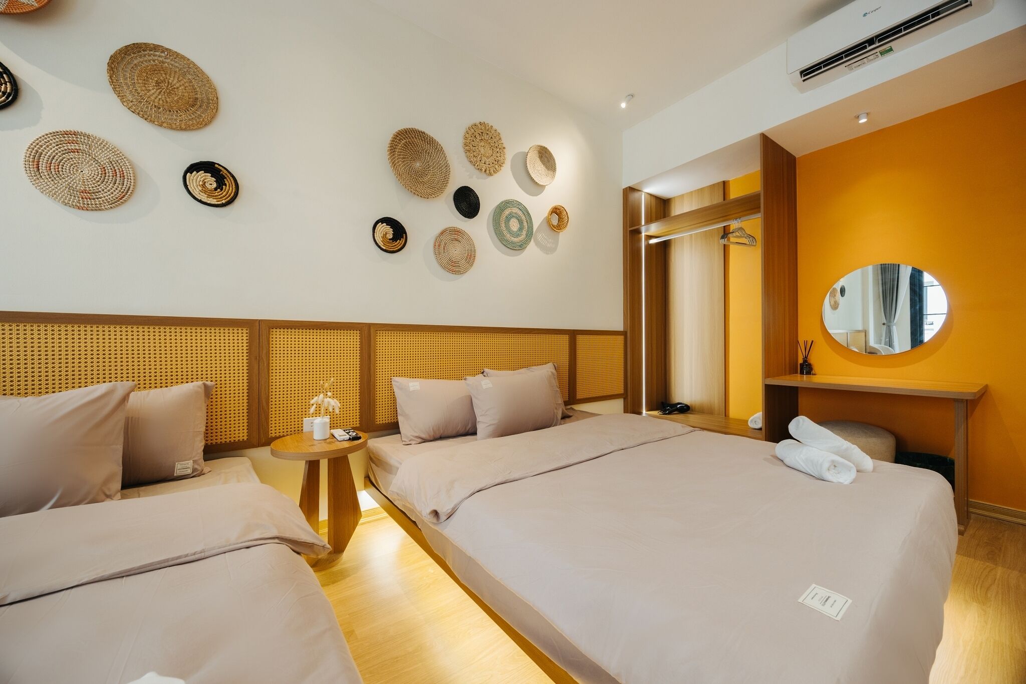 A hotel room with two beds, a round mirror, a small round table, and a wall with woven wall art.