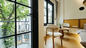 A modern room with large windows, a wooden floor, a bed, a chair, and a small table. - Moc Vien Homestay Train Street (Hanoi)