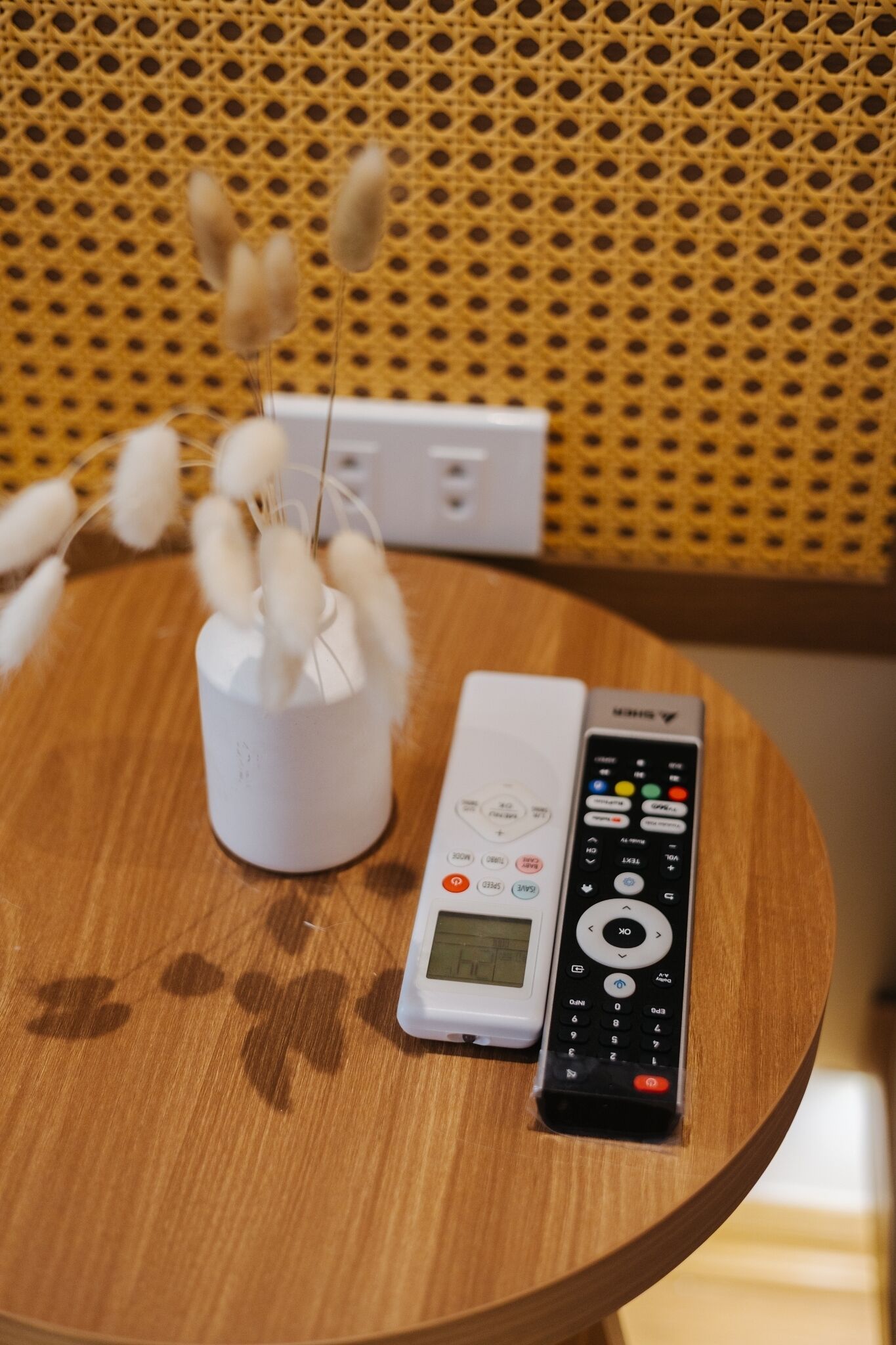 A white remote control and a white device on a wooden table with a woven background.
