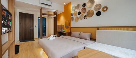 A hotel room with a bed, a sofa, a round table, a wall with woven baskets, and a hallway with a wooden floor and a door.