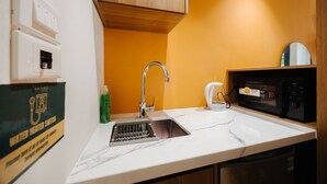 A kitchen with a sink, faucet, microwave, and a water heater switch on the wall. - Moc Vien Homestay Train Street (Hanoi)