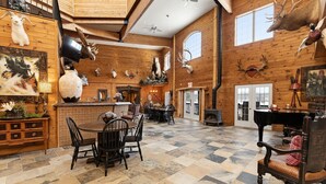 A spacious room with a large wooden ceiling, a fireplace, and a dining area with a table and chairs. - Whitestone Ranch | Luxury Lakefront Estate Near Muskoka (Sleeps 24) (Dunchurch)